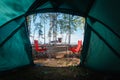 Camping in the middle of the forest, taken from inside the tent. View of the folding table and chairs with gas stove in the backgr