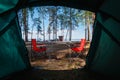 Camping in the middle of the forest, taken from inside the tent. View of the folding table and chairs with gas stove in the backgr