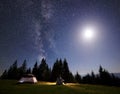 Camping night in mountain valley. Tourist sitting at tent enjoying starry sky and fool bright moon