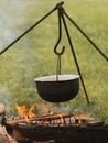 Camping outdoors. Cooking in a bowler hat hung on a tripod over a burning fire on the background of grass and chipped firewood