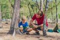 Camping people outdoor lifestyle tourists in summer forest near lazur sea. Blond boy son with father study survival