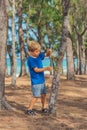 Camping people outdoor lifestyle tourists in summer forest near lazur sea. Blond serious boy in blue t-shirt study