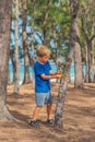 Camping people outdoor lifestyle tourists in summer forest near lazur sea. Blond serious boy in blue t-shirt study