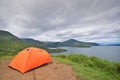 Camping in professional outdoor orange colour tent at the top of a hill overlooking dramatic lake view and cloud