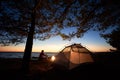 Woman having a rest at night camping near tourist tent, campfire on sea shore under starry sky Royalty Free Stock Photo