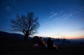 Camping site in mountains at dawn. Group of three tourists sitting in front of tent