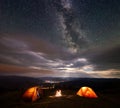 Camping tent on mountain at night under very starry sky against of luminous town