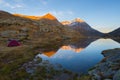 Camping with tent near high altitude lake on the Alps. Reflection of snowcapped mountain range and scenic colorful sky at sunset. Royalty Free Stock Photo