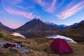 Camping with tent near high altitude lake on the Alps. Reflection of snowcapped mountain range and scenic colorful sky at sunset. Royalty Free Stock Photo