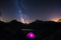 Camping under starry sky and milky way at high altitude on the Alps. Illuminated tent in the foreground and majestic mountain peak