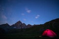Camping under starry sky and milky way at high altitude on the Alps. Illuminated tent in the foreground and majestic mountain peak Royalty Free Stock Photo