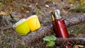 Camping utensils for picnic in the forest. Red metal thermos and plastic mugs for making coffee and tea on a hike Royalty Free Stock Photo