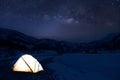 Camping in the wilderness. A pitched tent under the glowing night sky stars of the milky way with snowy mountains. Milky Way and M Royalty Free Stock Photo