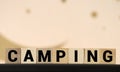 Camping word on a wooden cube sign with a blurry background of a campsite in the summer