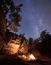 Campsite at night. Young tourist couple, man and woman standing near small tent lit by burning fire Royalty Free Stock Photo