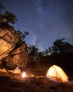 Campsite night. Girl sitting on boulder watching bonfire in front of tourist tent