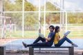 On a campus, a couple of students are studying together, and a teenager sits on a seat beside a sports court with a book Royalty Free Stock Photo