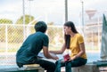 On a campus, a couple of students are studying together, and a teenager sits on a seat beside a sports court with a book Royalty Free Stock Photo