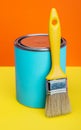 Can of blue paint and paintbrush on orange and yellow background Royalty Free Stock Photo