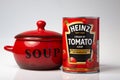 a can of Heinz tomato soup next to a red soup bowl on a white background