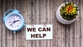 We can help text on a sticker, a flower in a pot and an alarm clock Royalty Free Stock Photo
