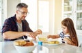 Can I help you. an adorable little girl having breakfast with her father in the kitchen. Royalty Free Stock Photo