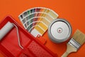 Can of paint, brush, roller, container and color palette samples on orange background, flat lay Royalty Free Stock Photo