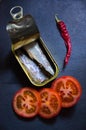 Can of sardines, some tomato slices and a chilli on a black slate Royalty Free Stock Photo