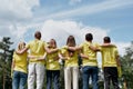 We can save the planet together. Group of young volunteers wearing uniform and rubber gloves hugging and looking at