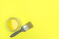 Can of yellow paint with grey paintbrush on yellow background