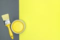 Can of yellow paint with yellow paintbrush on yellow-gray background.