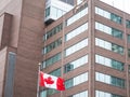 Canada Wordmark, the official logo of the Canadian government, on an administrative building next to a Canadian flag waiving Royalty Free Stock Photo