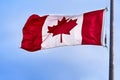 Canadian flag flying in light breeze on top of metal pole against blue sky Royalty Free Stock Photo