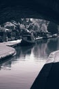 Canal with barges moored outside residential buildings. Taken underneath an old stone bridge.