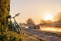 Canal boat with mountain bike left leaning against hedge row early morning sunrise dawn with golden light in sky on River Trent