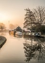 Canal narrow river boats at foggy dawn sunrise with beautiful mist orange haze wood burning smoke from chimneys silhouette trees