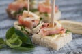 Canape with Salmon Fish Pieces, Butter Cream, White Bread and Arugula Leaves. European food. Wooden Gray Background.