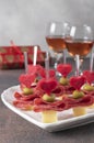 Canape for Valentines Day with hearts from cheese, olives and sausage on white plate shaped-heart and two glass rose