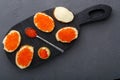 Canapes with butter and red caviar next to a spoon with caviar on a wooden board on a concrete background. Royalty Free Stock Photo