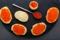 Canapes with butter and red caviar and a tartlet and a spoon with caviar on a black board on a concrete background