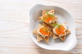 Canapes with red caviar on toasted bread in star shape with cream and dill garnish on a white plate, light wooden table, copy