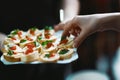 Canapes, sandwiches with caviar salmon on square crackers on a white plate, extending a hand to taste Royalty Free Stock Photo