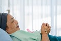 Cancer patient during chemotherapy treatment with headscraf and ink ribbon on shirt lying on hospital bed with cross on hand to Royalty Free Stock Photo