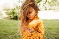 Candid closeup portrait of cute little girl have seriously face during looking to her fingers, osing at nature background.