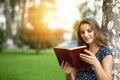 Woman sitting outside near a tree reading a book smiling Royalty Free Stock Photo