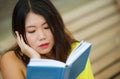 Candid lifestyle portrait of young beautiful and relaxed Asian Korean student girl on reading book or studying outdoors at coffee Royalty Free Stock Photo