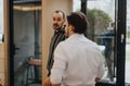 A candid moment as two men engage in a conversation, seen through a reflection in a glass doorway, capturing a sense of