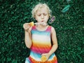 Cute funny little blonde Caucasian child girl lying on ground grass blowing soap bubbles in park Royalty Free Stock Photo