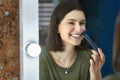 Candid portrait of a happy brunette young woman looking to the mirror and making makeup herself Royalty Free Stock Photo