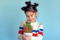 Candid portrait of a pretty smiling positive little girl holds cactus in hands posing on studio blue color background. Cute Royalty Free Stock Photo